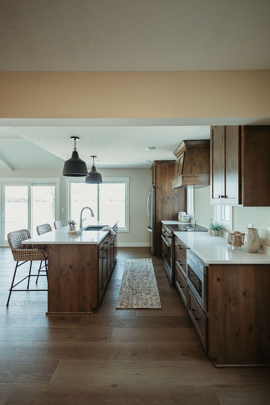 Modern kitchen with a wooden island, pendant lights, and a long white countertop by a bright window.
