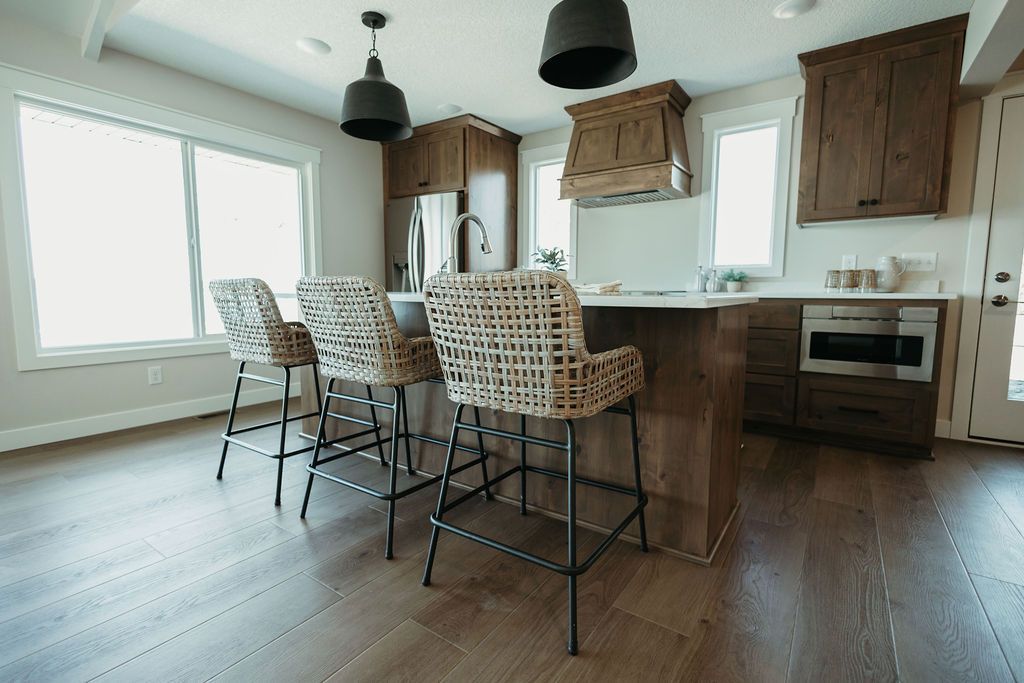 Modern kitchen with a wooden island, woven bar stools, dark floor, and large windows