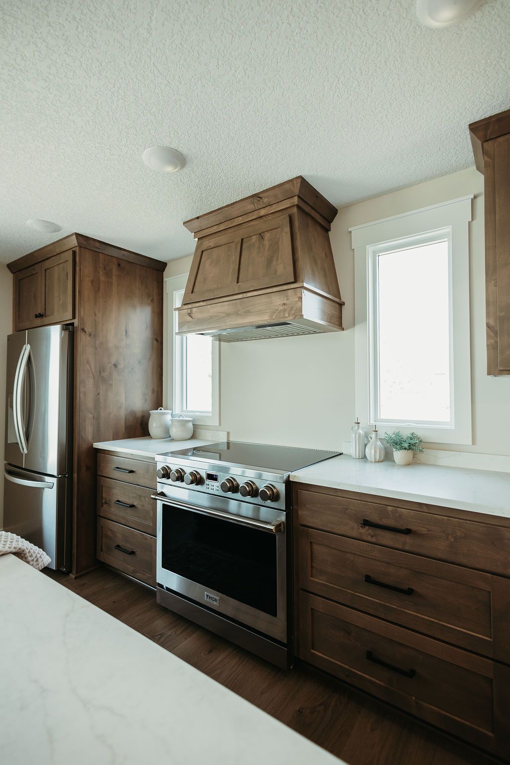 Modern kitchen with wood cabinets, stainless stove, white countertops, and two bright windows