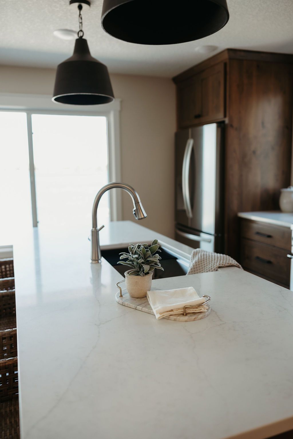 Modern kitchen with white island, pendant lights, stainless fridge, and a vase centerpiece.
