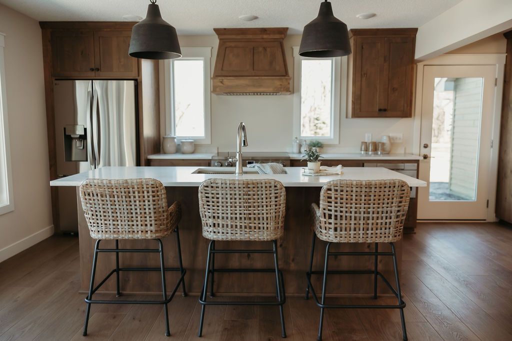 Modern kitchen with island, three woven bar stools, pendant lights, and hardwood floors