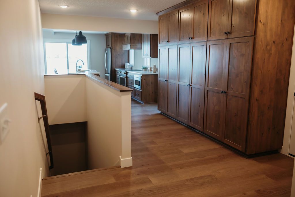 Bright hallway with wood floors, built-in wooden cabinets, and a stairwell opening on the left.