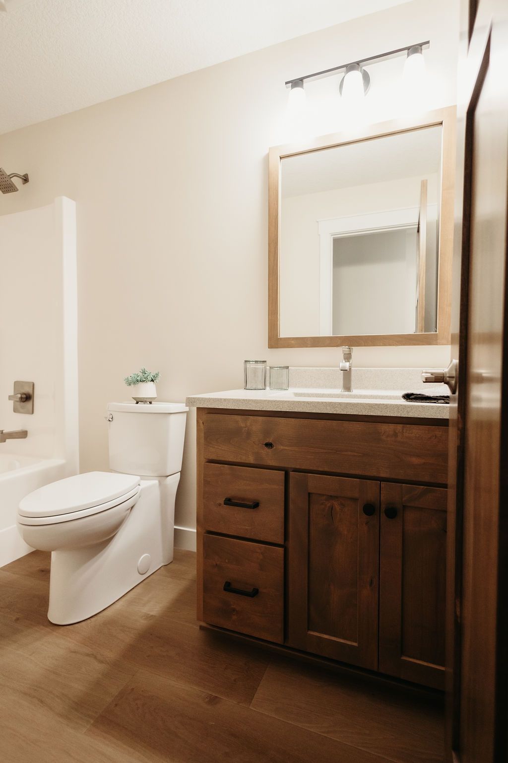 Modern bathroom with dark wood vanity, mirror, toilet, and beige walls and floor