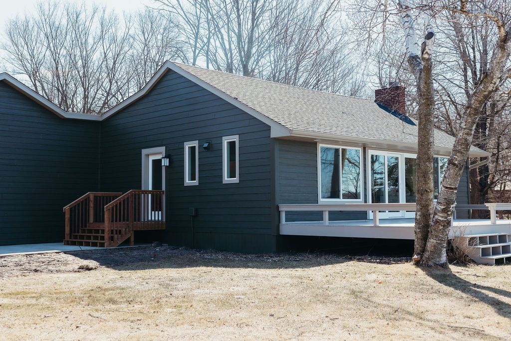 Dark blue house with white trim, small porch, and large windows in a snowy yard