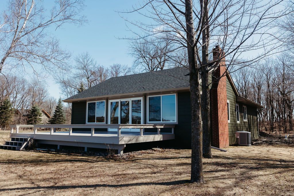 Small cabin with a deck in a leafless wooded yard under a clear blue sky