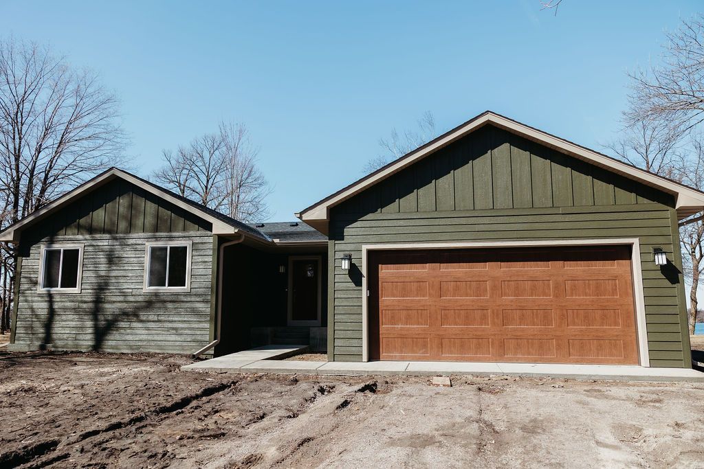 Suburban house with green siding and a two-car garage under a clear blue sky