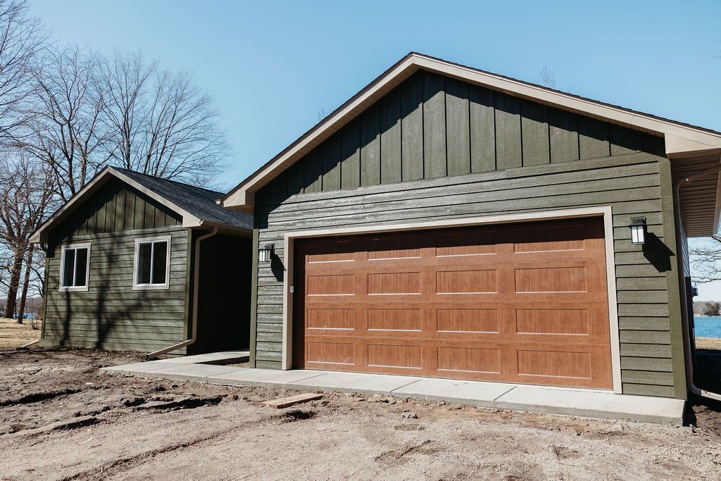 Detached garage and small house with green siding and a brown garage door in a rural setting