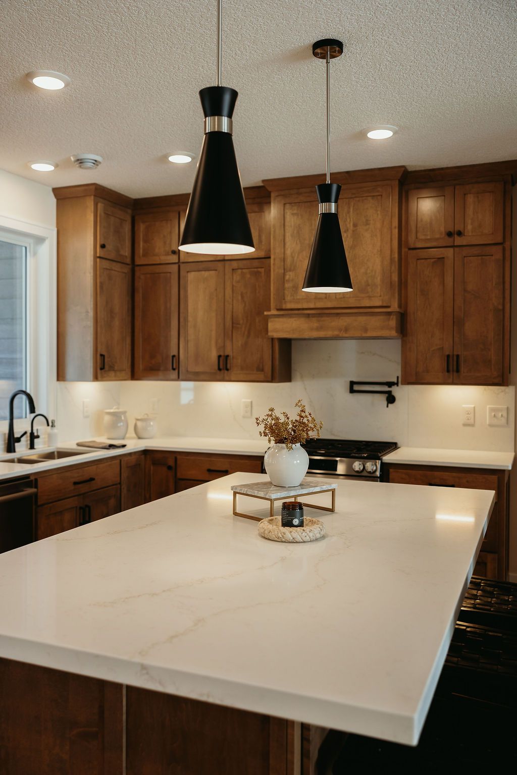 Modern kitchen with wood cabinets, white countertops, and black pendant lights.