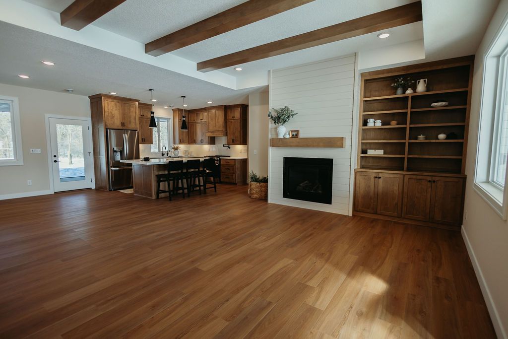 Spacious open-plan living room with hardwood floors, exposed beams, fireplace, and kitchen bar seating
