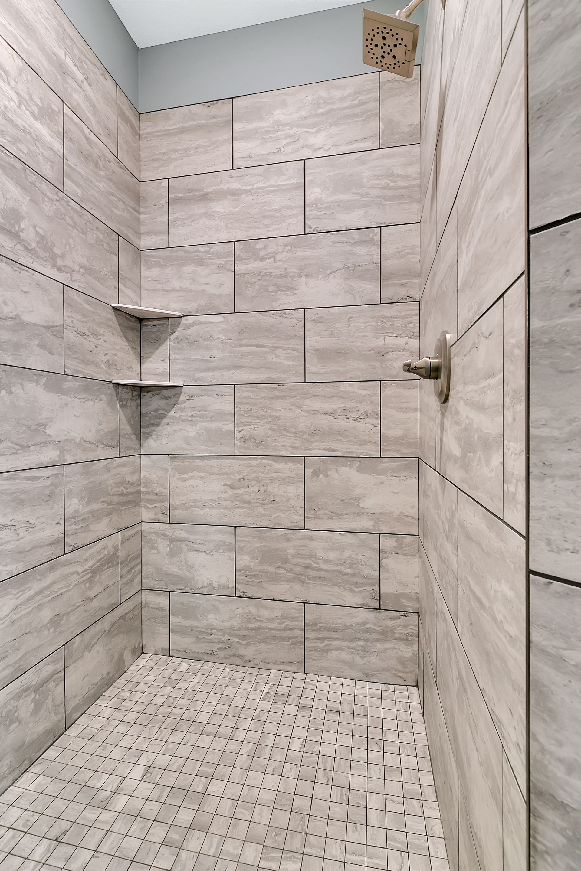 A walk in shower with tiled walls and a mosaic floor.