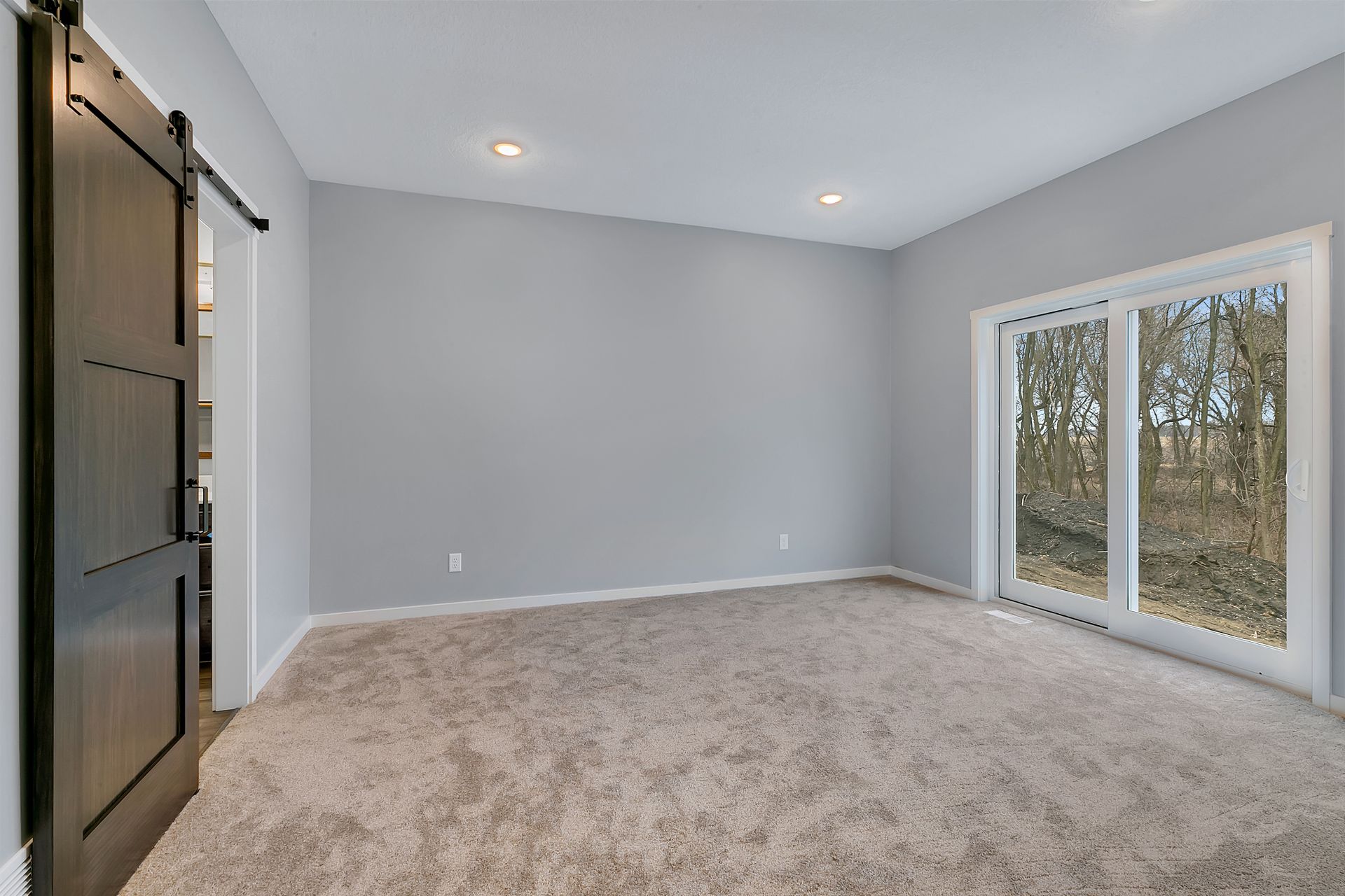 An empty room with a barn door and sliding glass doors.