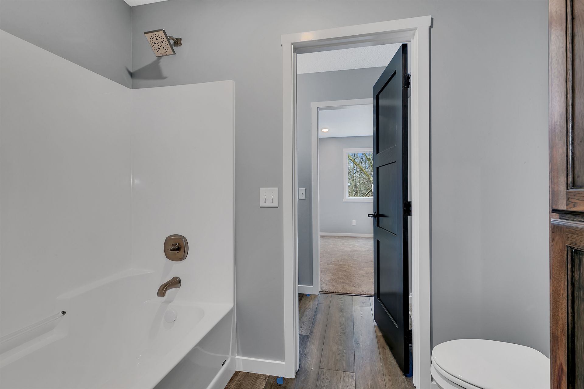 A bathroom with a bathtub , toilet , and door leading to a bedroom.