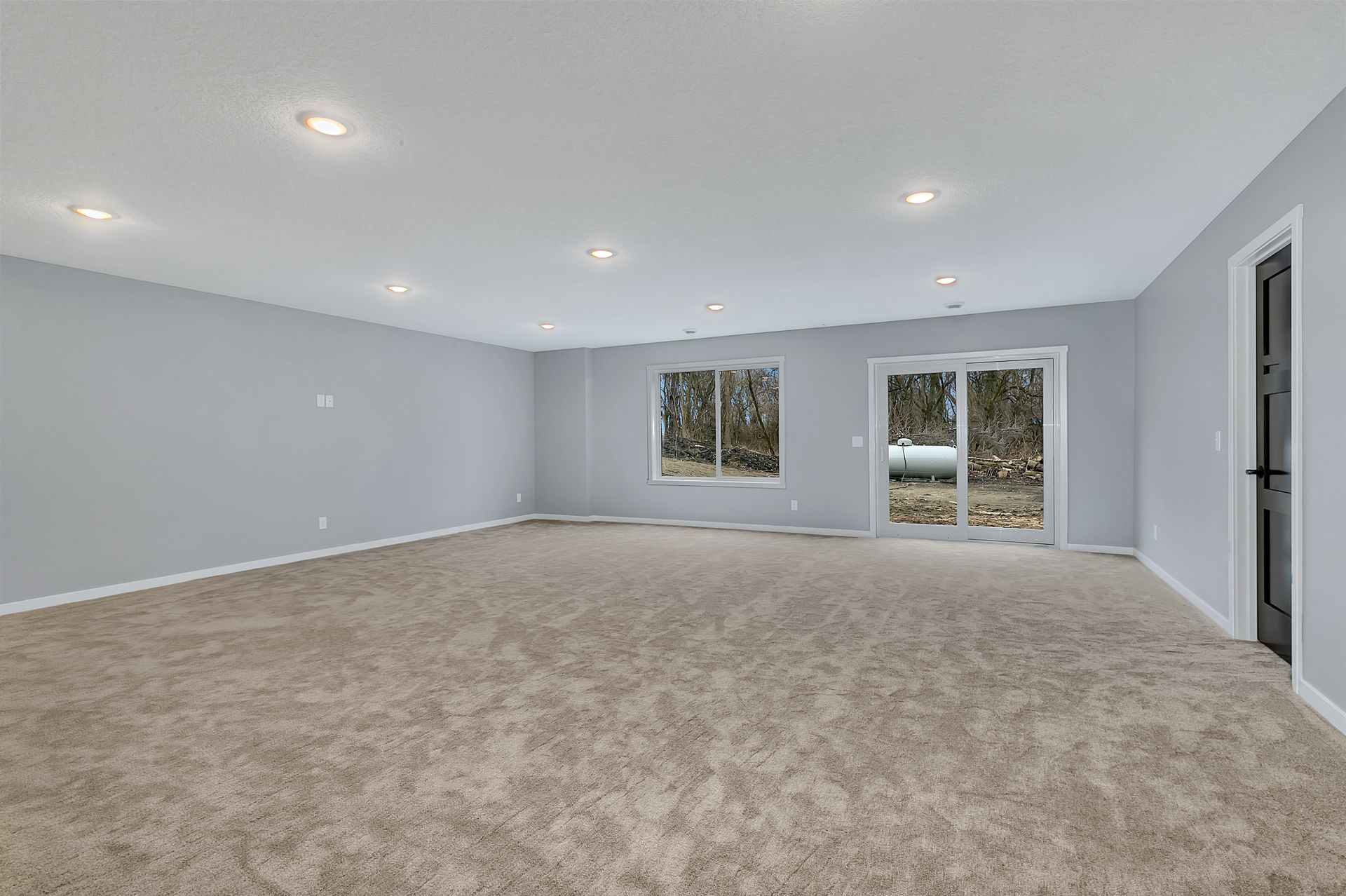 A large empty room with a carpeted floor and sliding glass doors.