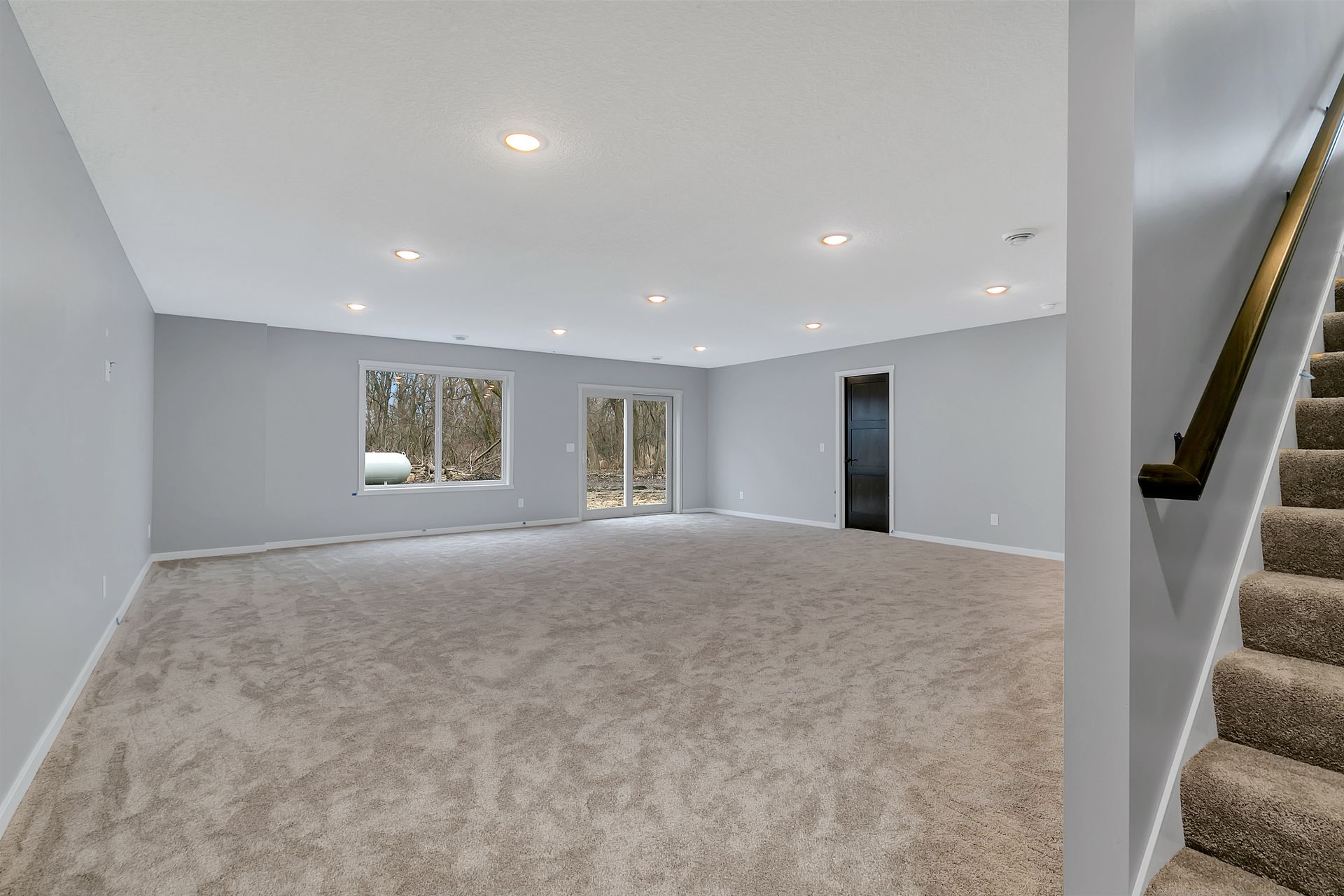 An empty basement with carpeted floors and stairs leading up to the second floor.