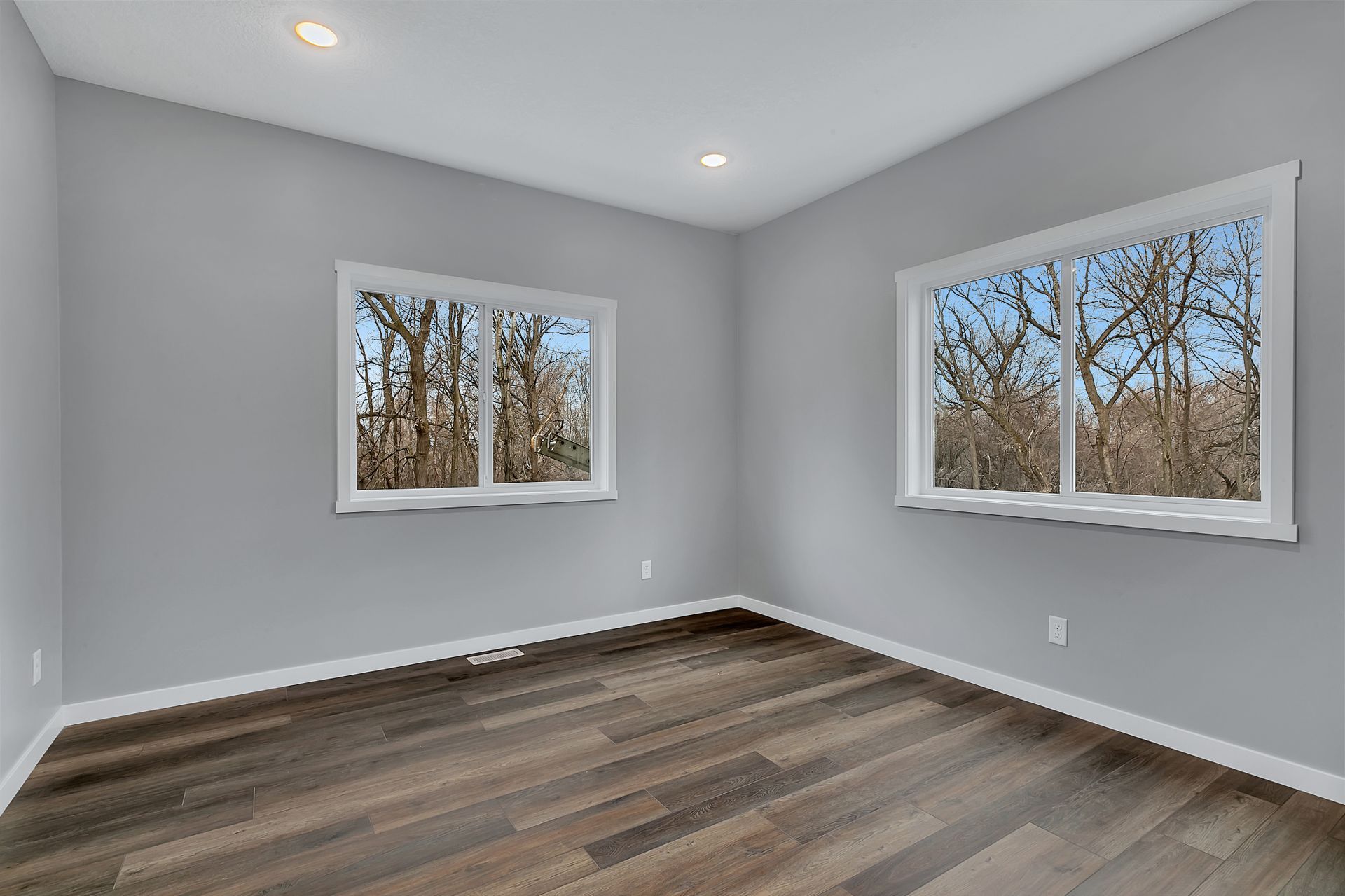 An empty room with hardwood floors and two windows.