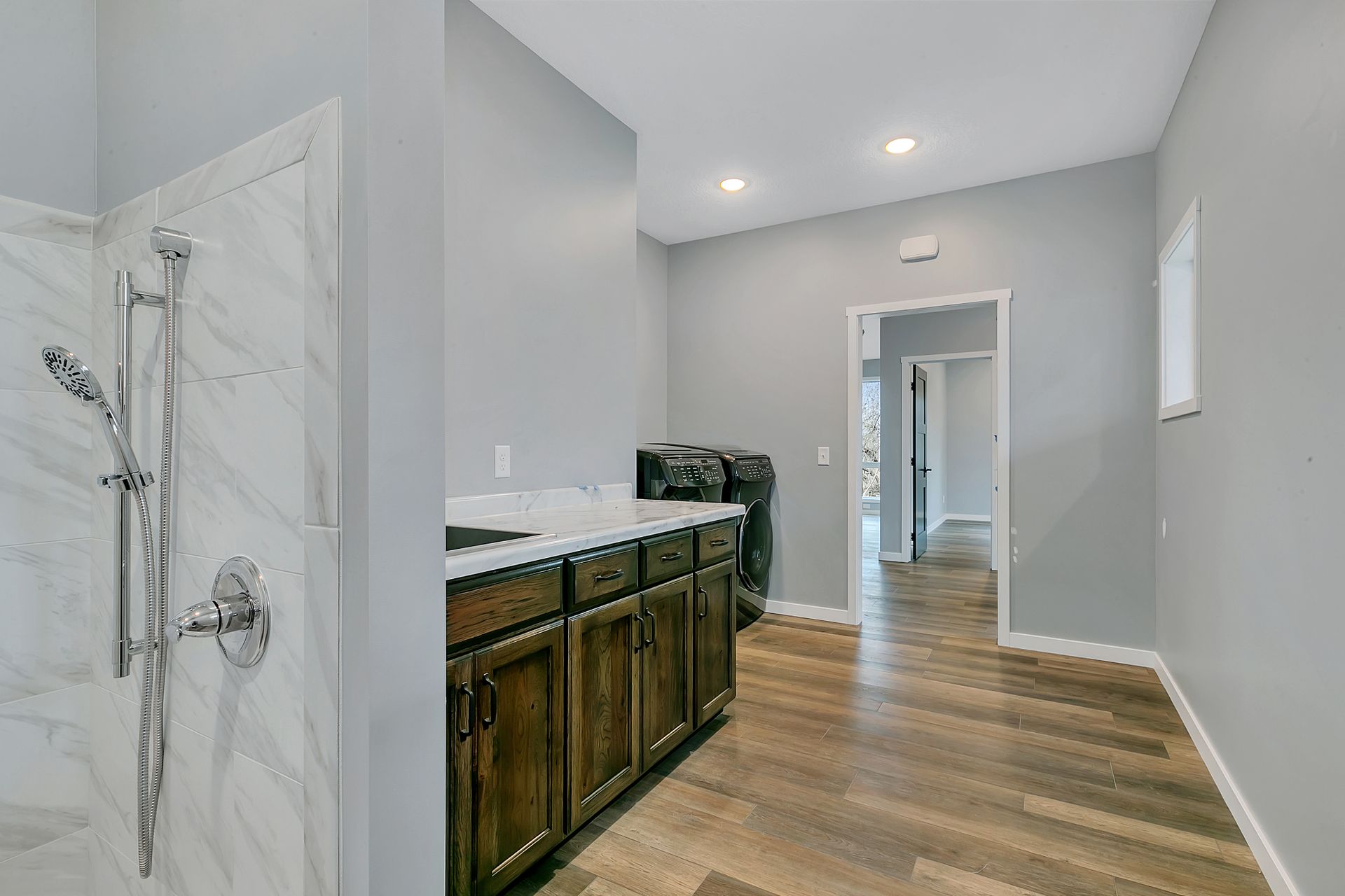 A bathroom with a shower , sink , cabinets and hardwood floors.