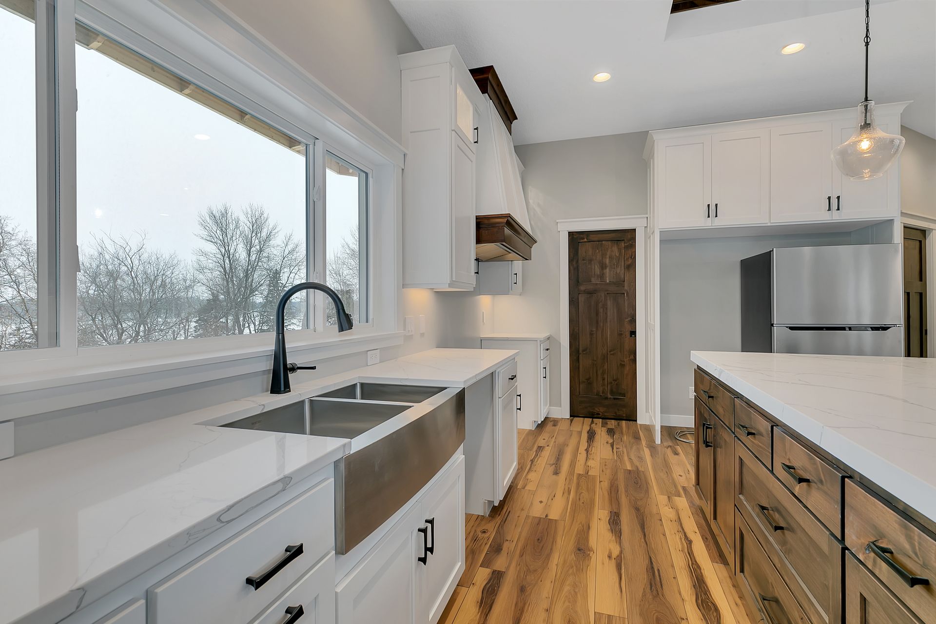 A kitchen with white cabinets , stainless steel appliances , a sink , and a large window.