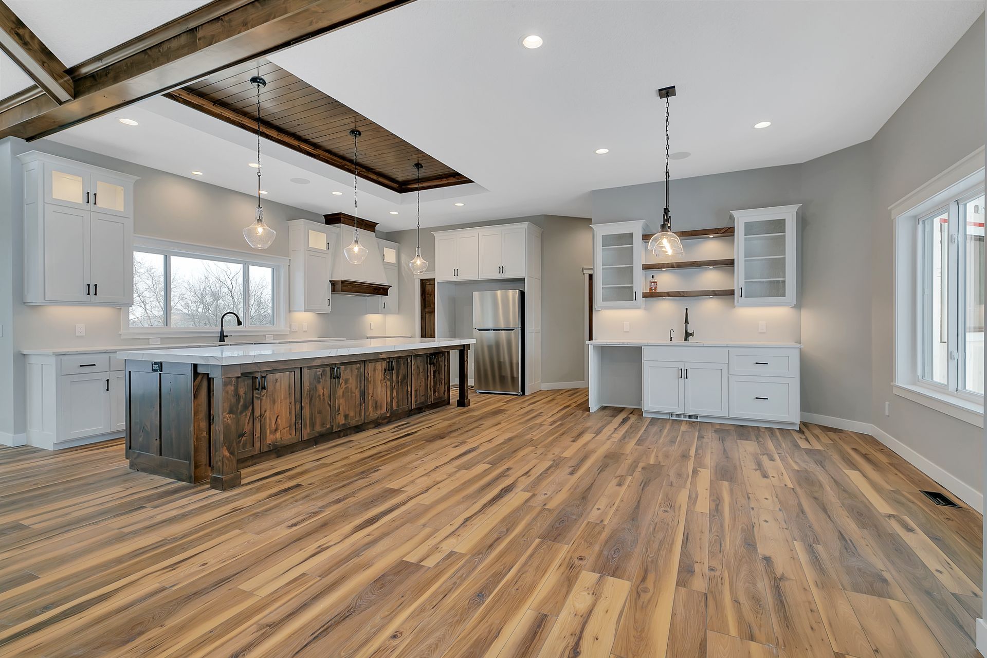 A kitchen with wooden floors , white cabinets , and a large island.