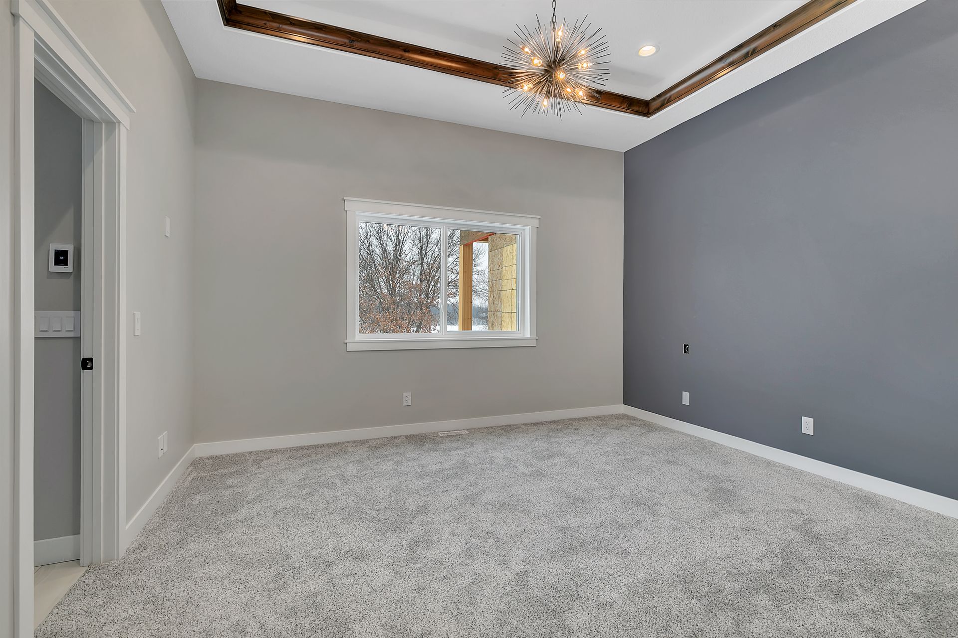 An empty bedroom with a large window and a chandelier.