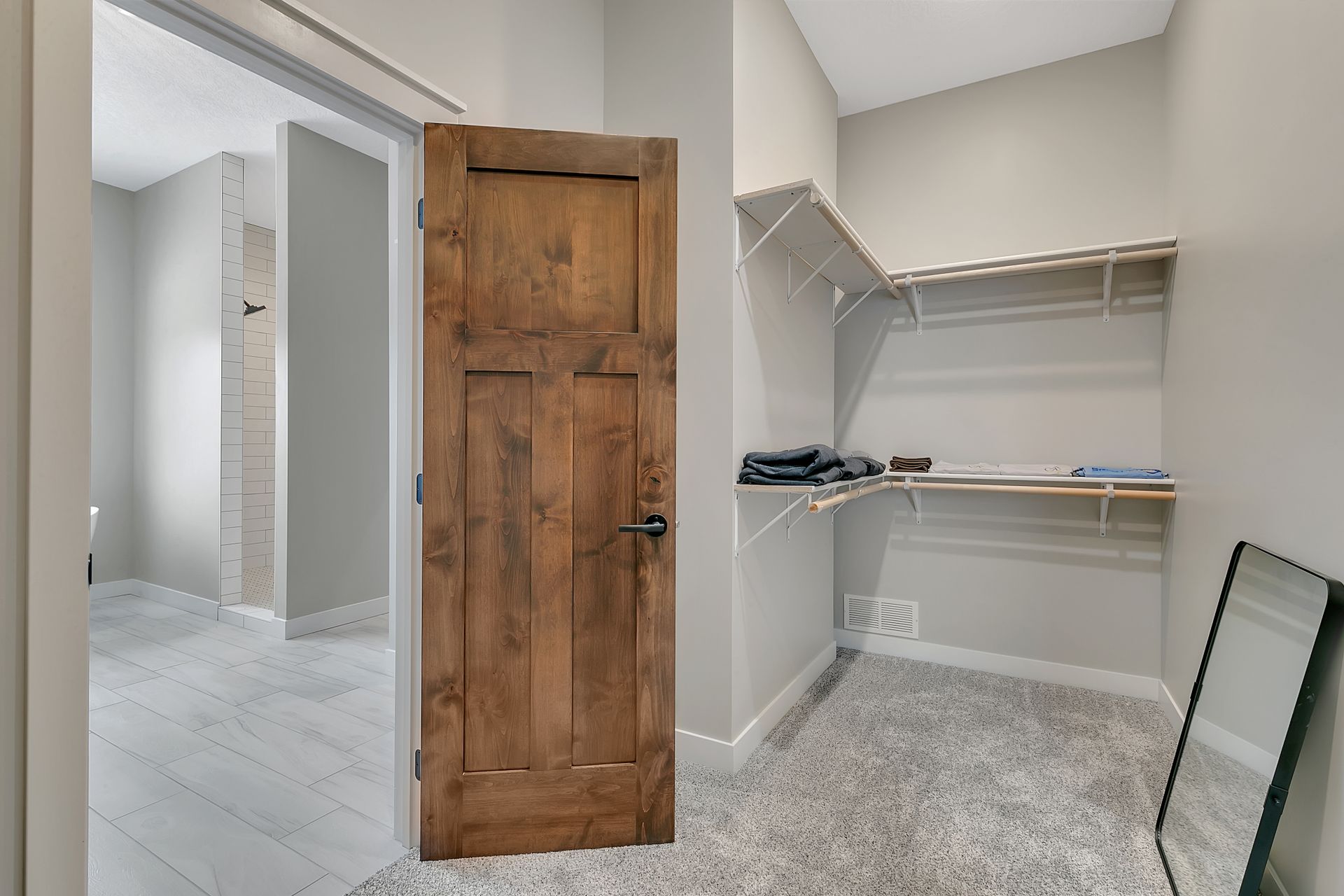 A walk in closet with a wooden door and a mirror.