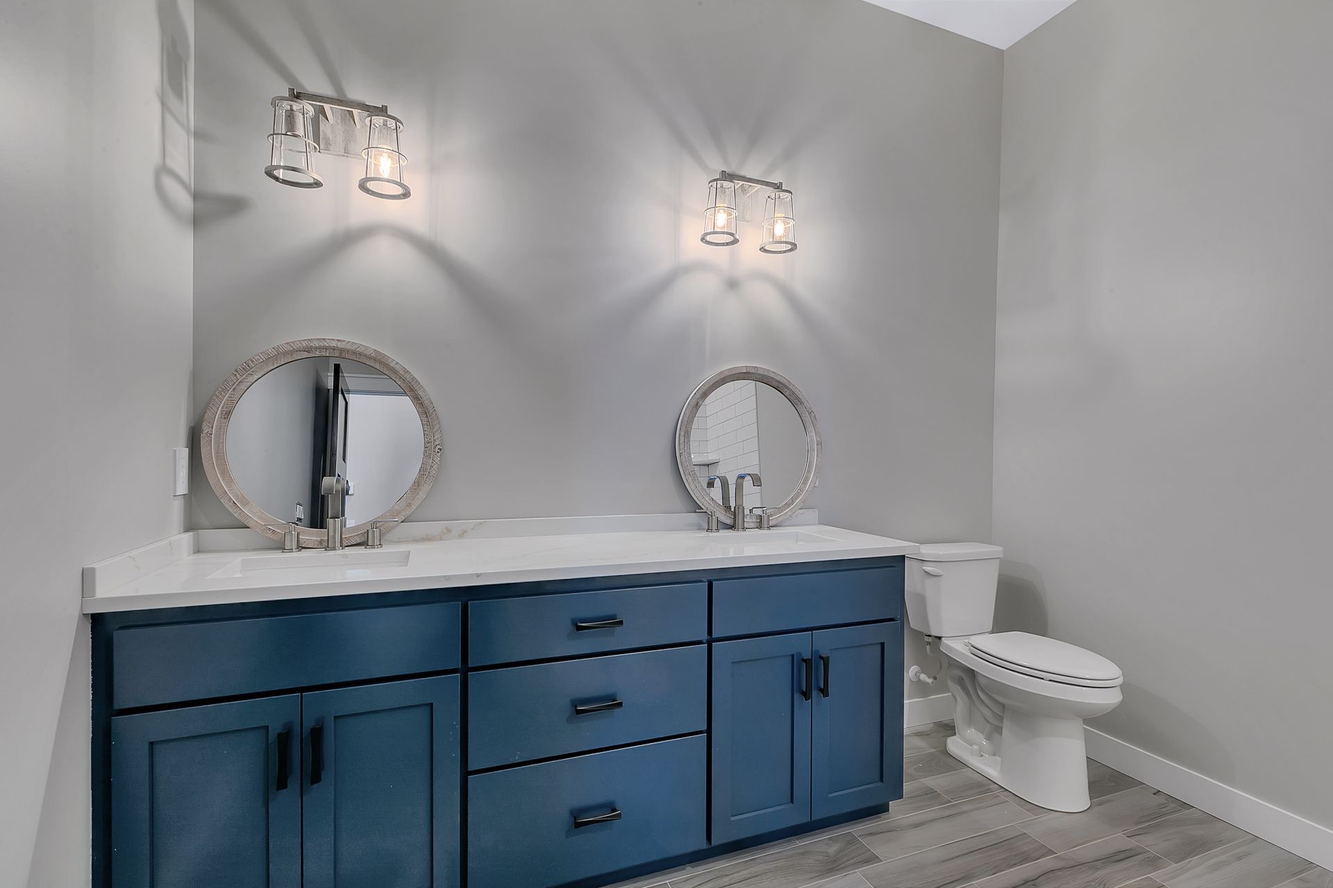 A bathroom with blue cabinets , a toilet , a sink and two mirrors.