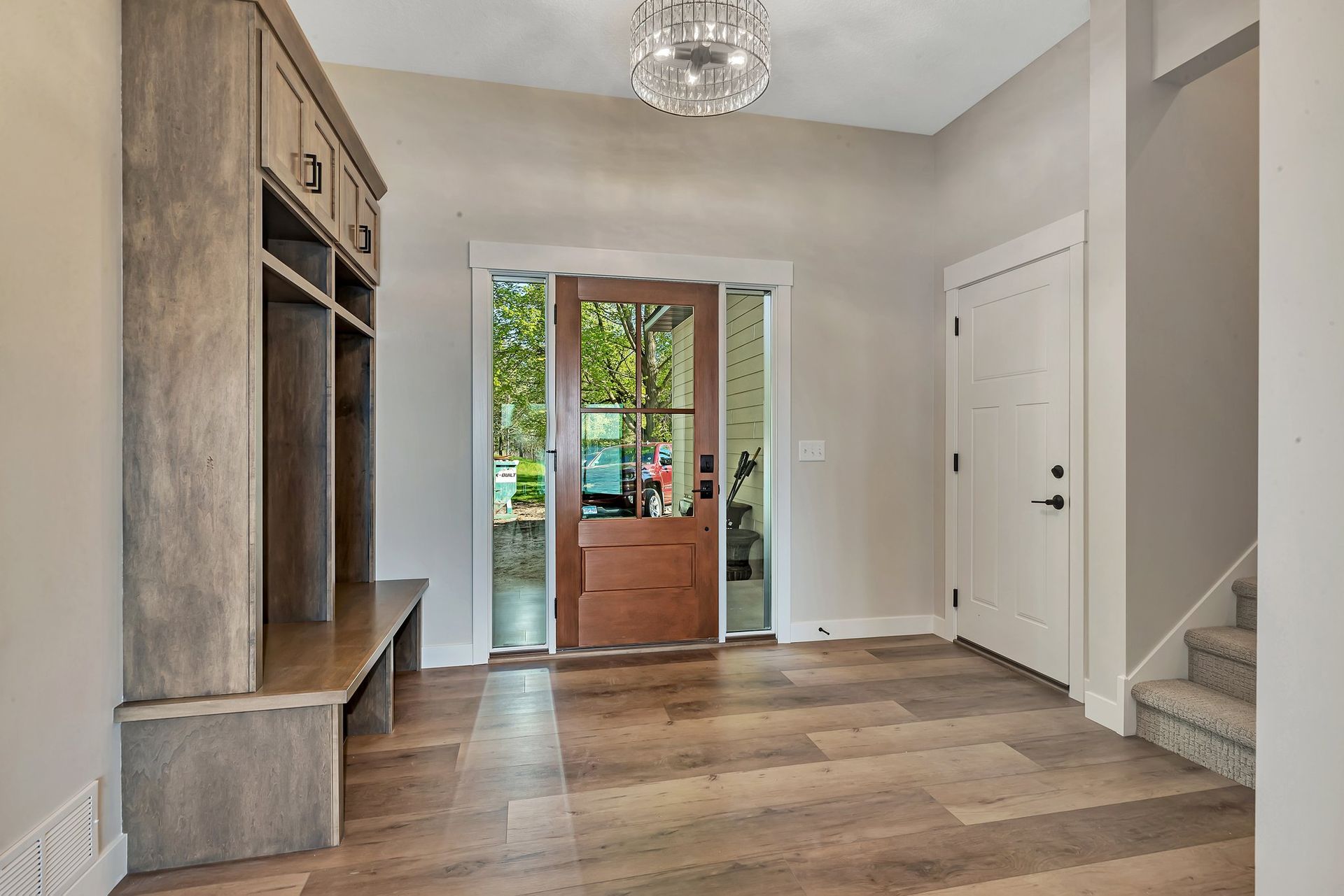 A hallway with hardwood floors , a wooden door , stairs and a chandelier.