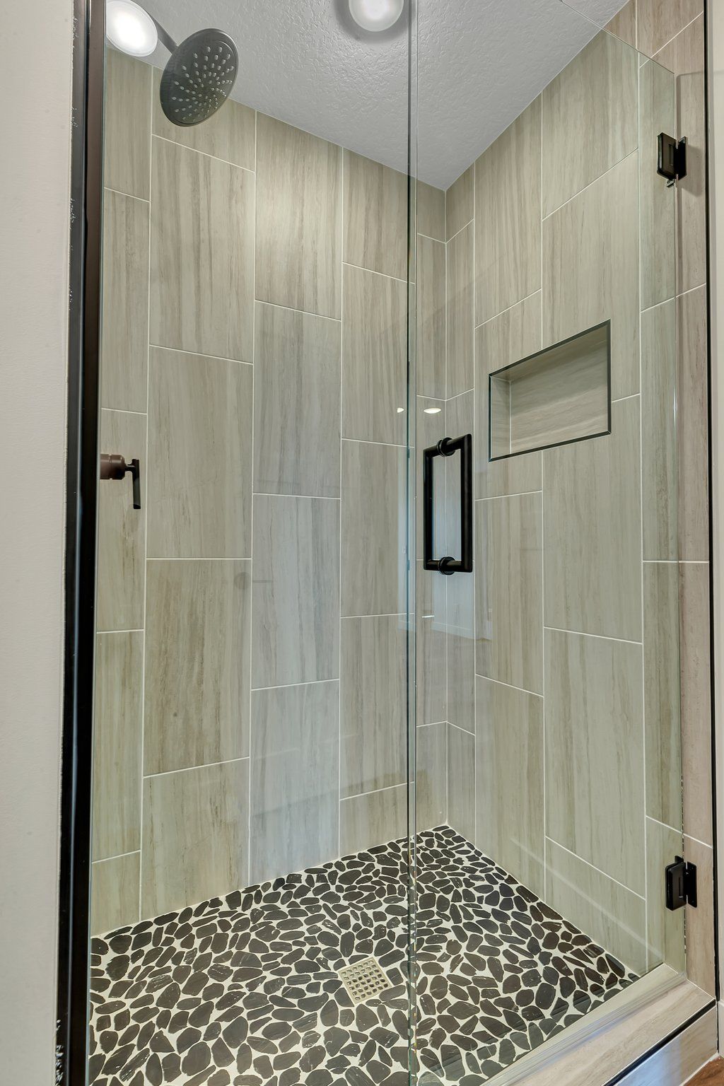 A walk in shower with a tiled floor and a glass door.