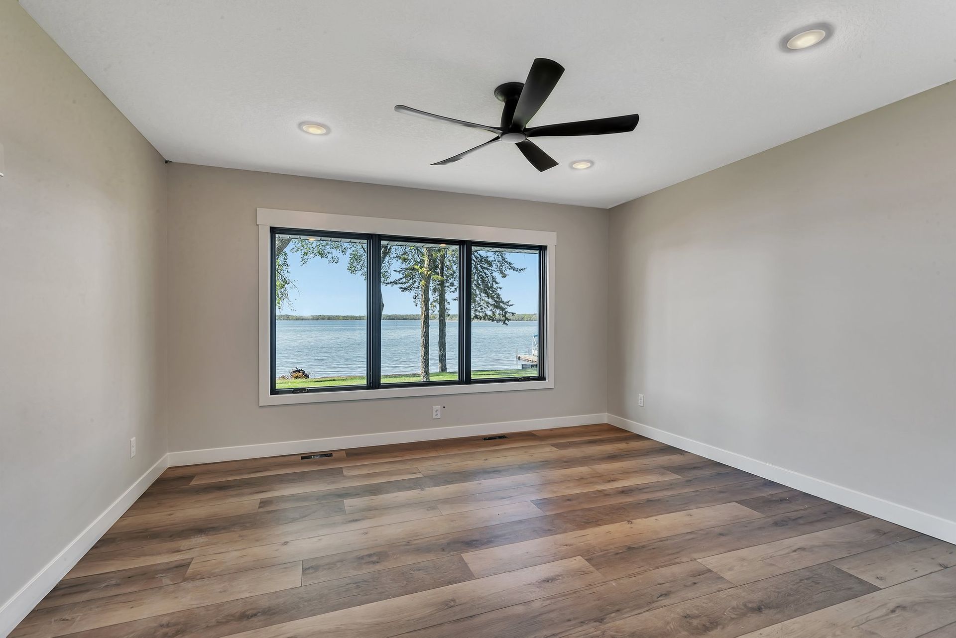 There is a ceiling fan in the room and a large window with a view of the water.