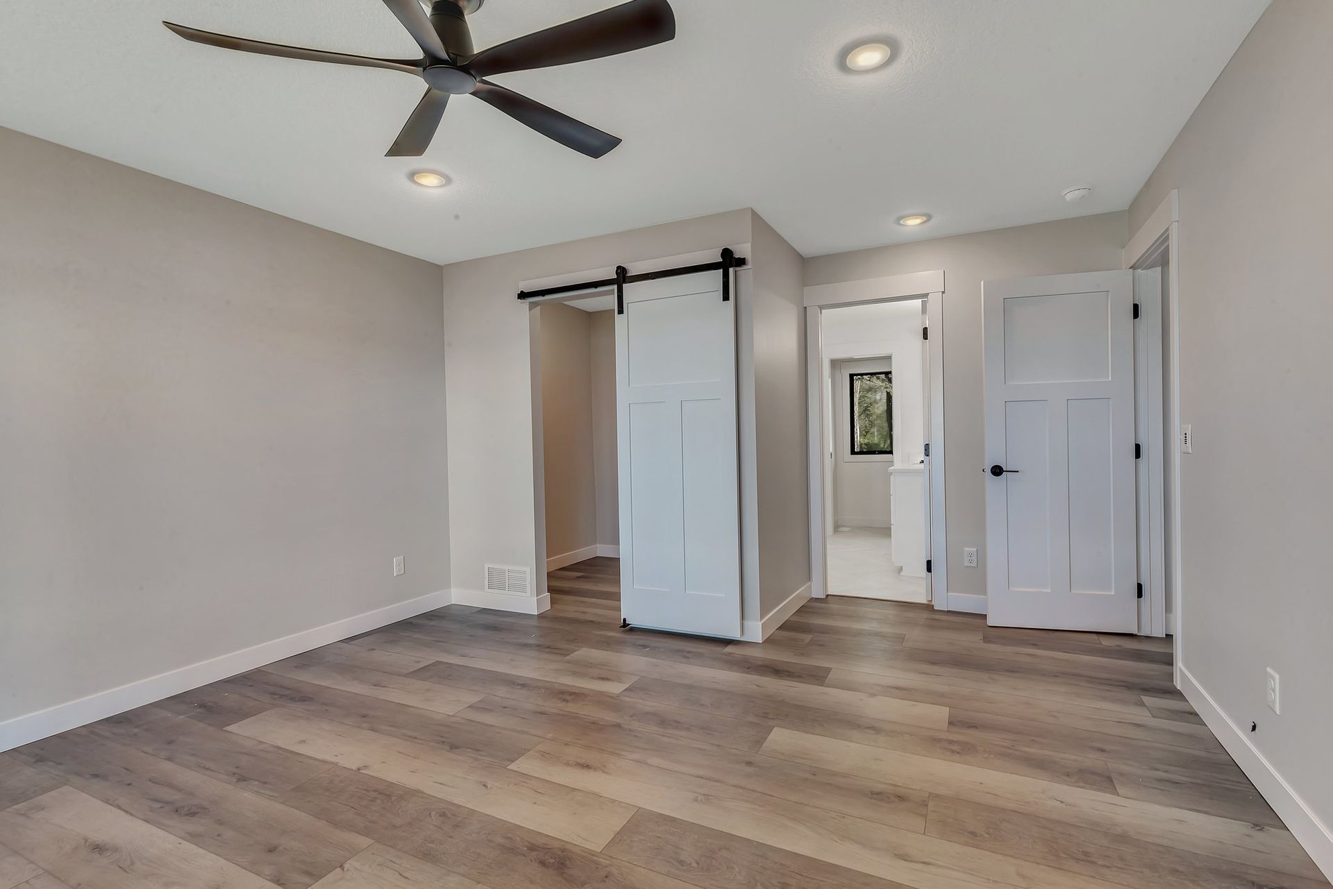 An empty bedroom with a ceiling fan and sliding barn doors.