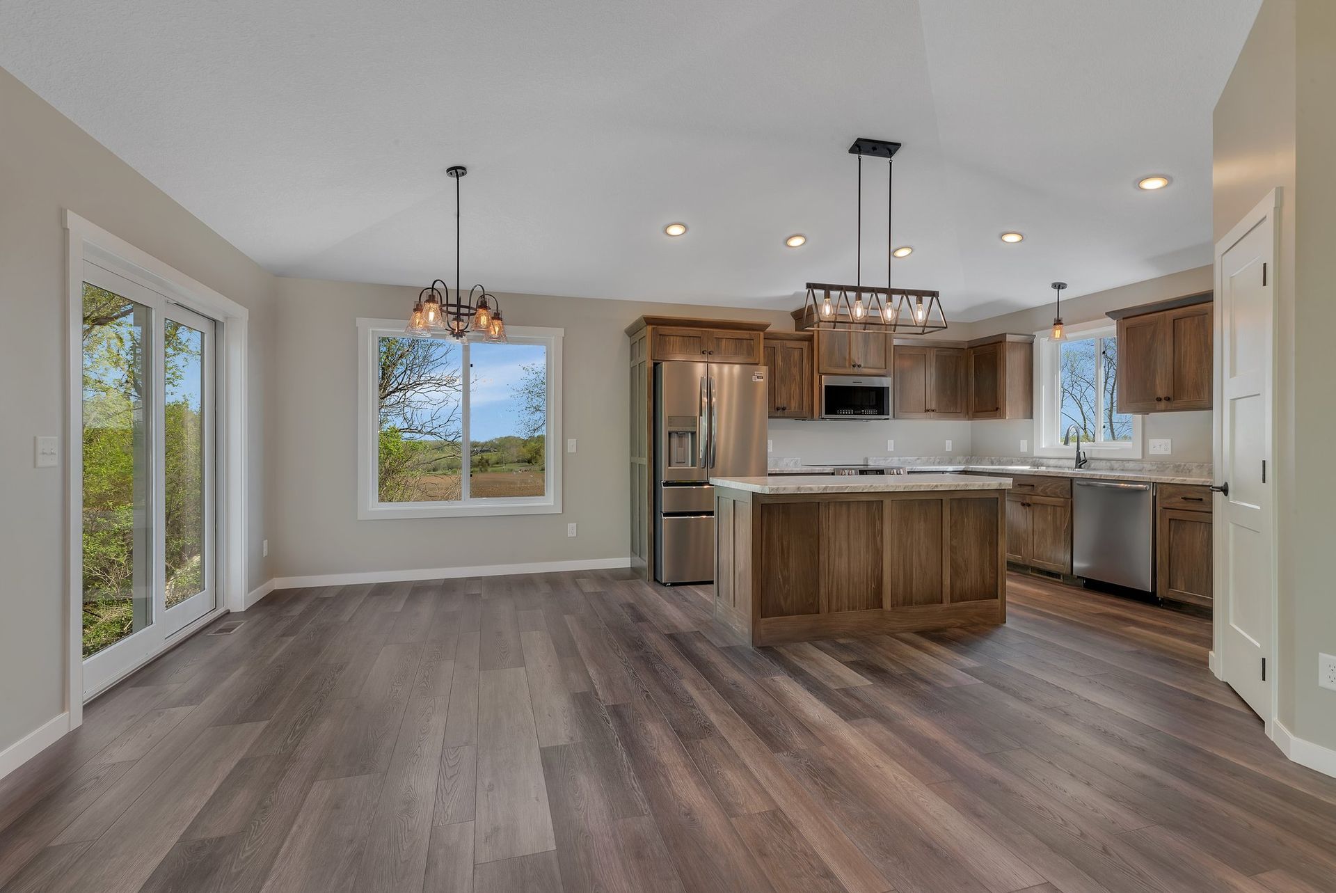 A large empty room with hardwood floors and stainless steel appliances in a house.
