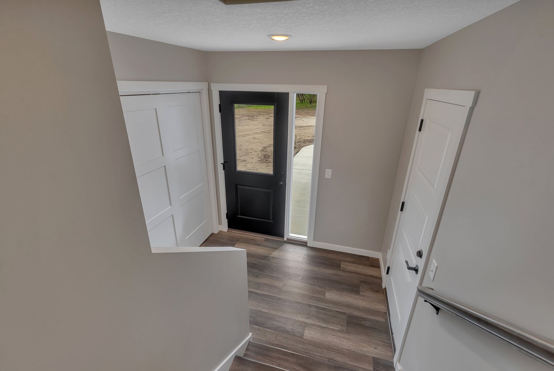 A hallway with a black door and stairs leading up to it.