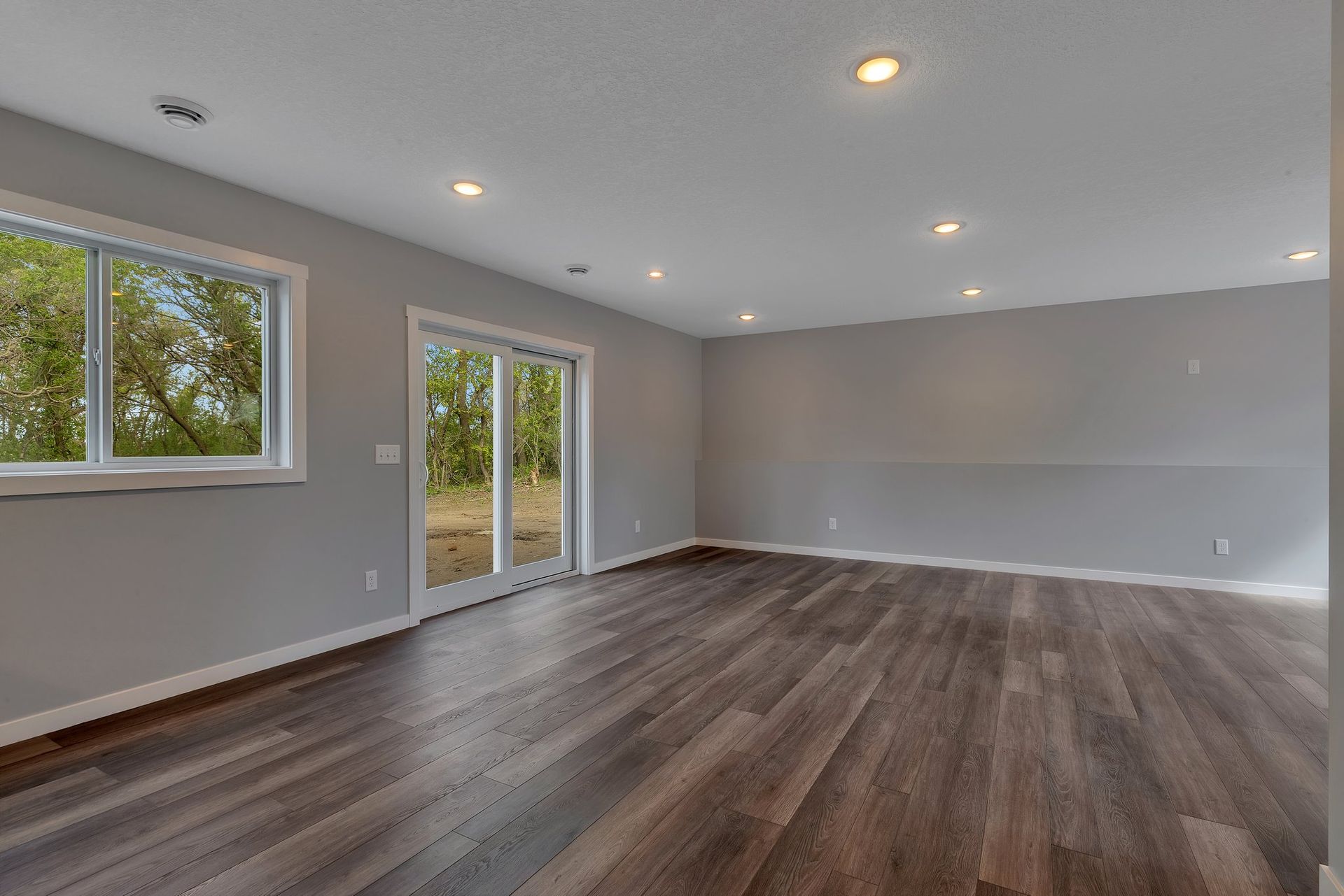 An empty living room with hardwood floors and sliding glass doors.