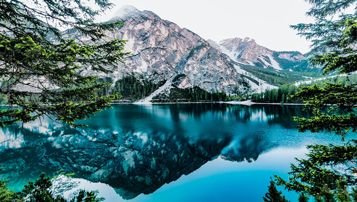 A lake surrounded by mountains and trees with a reflection of the mountains in the water.