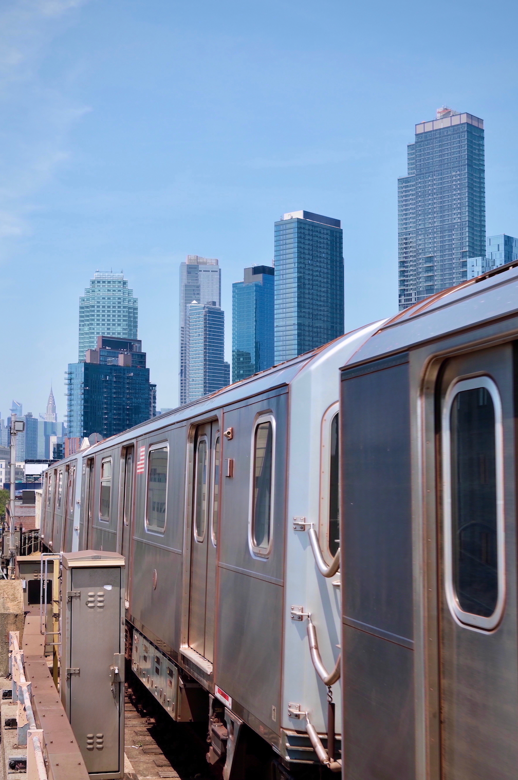 A subway train is pulling into a station with a city skyline in the background.
