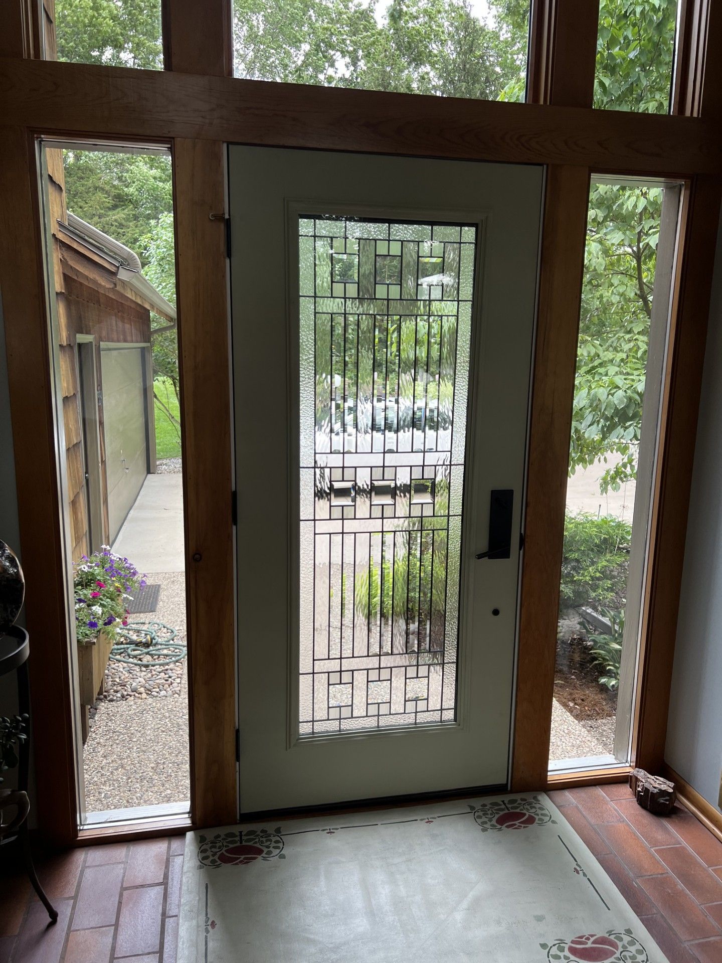 Front door with glass panel and metal security screen, looking out to a tree-lined porch and driveway