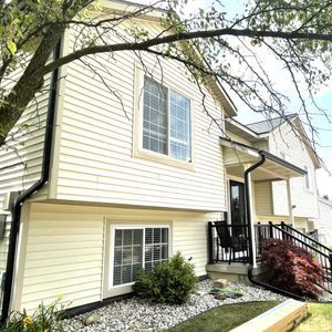 A two-story house with light yellow siding, black gutters, and a front porch with a black railing.