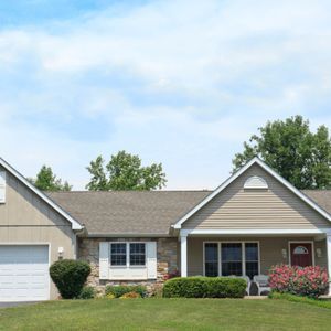 Tan ranch-style house with a white garage door and a red front door on a sunny day.