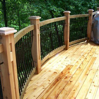 Wooden deck with curved railing, black spindles, and surrounding trees.