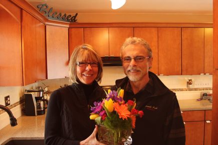 A man and a woman holding a vase of flowers in a kitchen