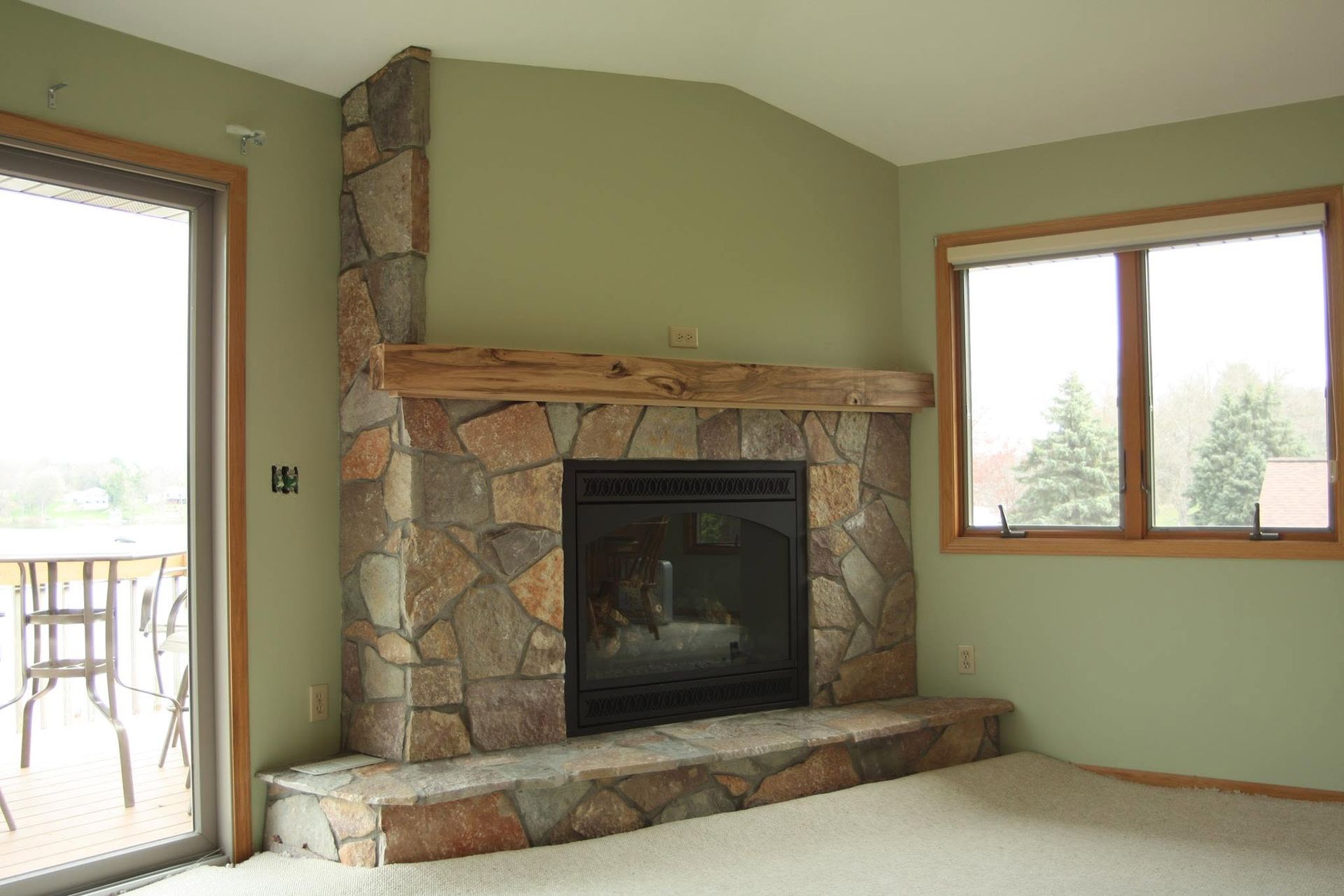 Empty living room with stone fireplace, beige carpet, and two windows.