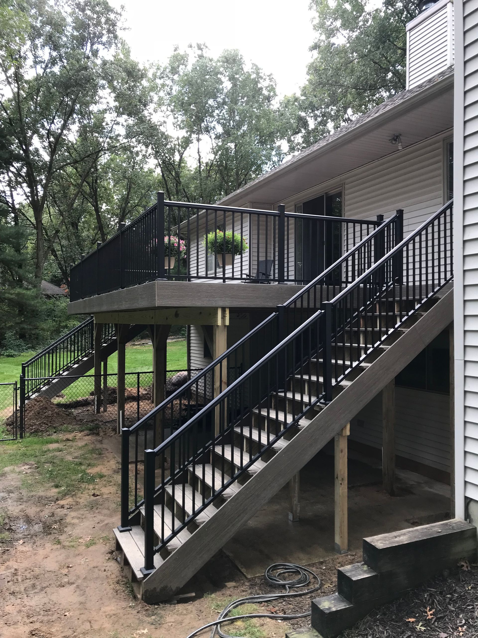 Backyard deck with black stairs and railing beside a white house, surrounded by trees