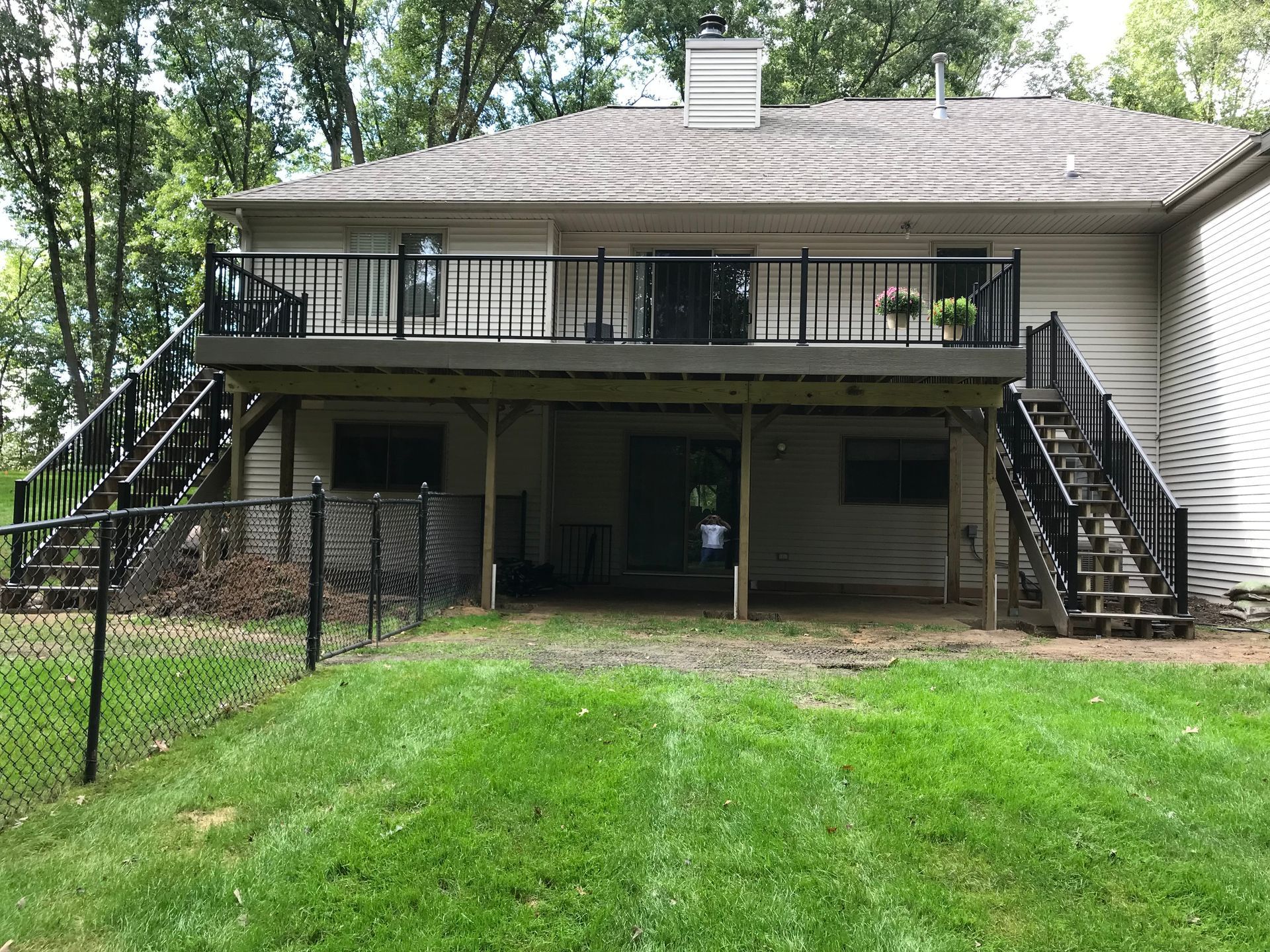 Backyard view of a raised house with stairs, deck, and green lawn.