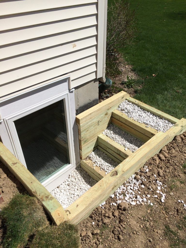 A wooden staircase leading to a window in the basement of a house.