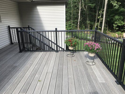 A wooden deck with black railings overlooking a backyard with trees, featuring two potted plants on metal stands.