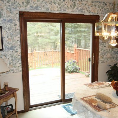 Sliding glass door with brown wooden frame leading to a deck with trees; view from interior with wallpaper.