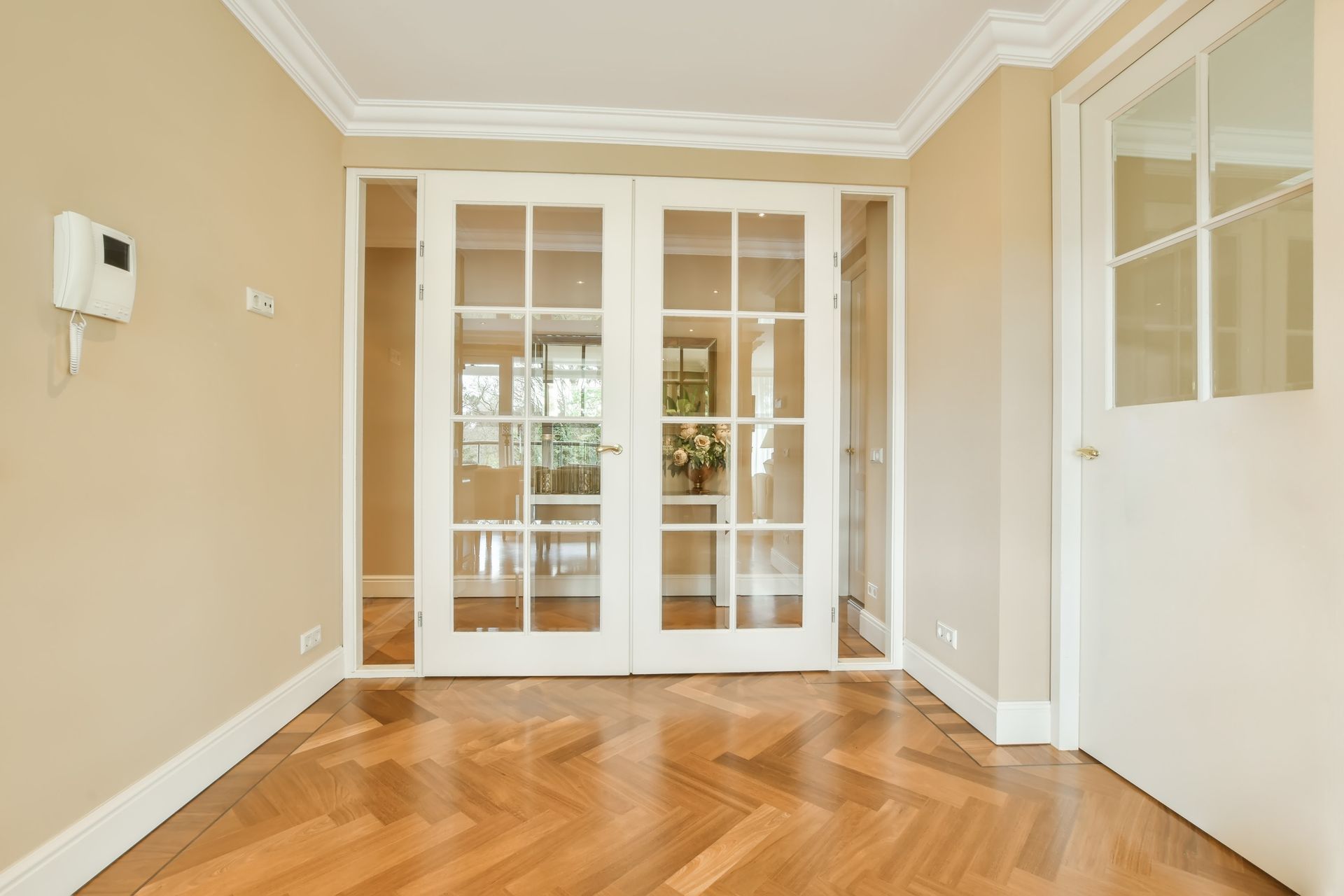 Empty beige room with hardwood floors and glass double doors opening to a brighter space
