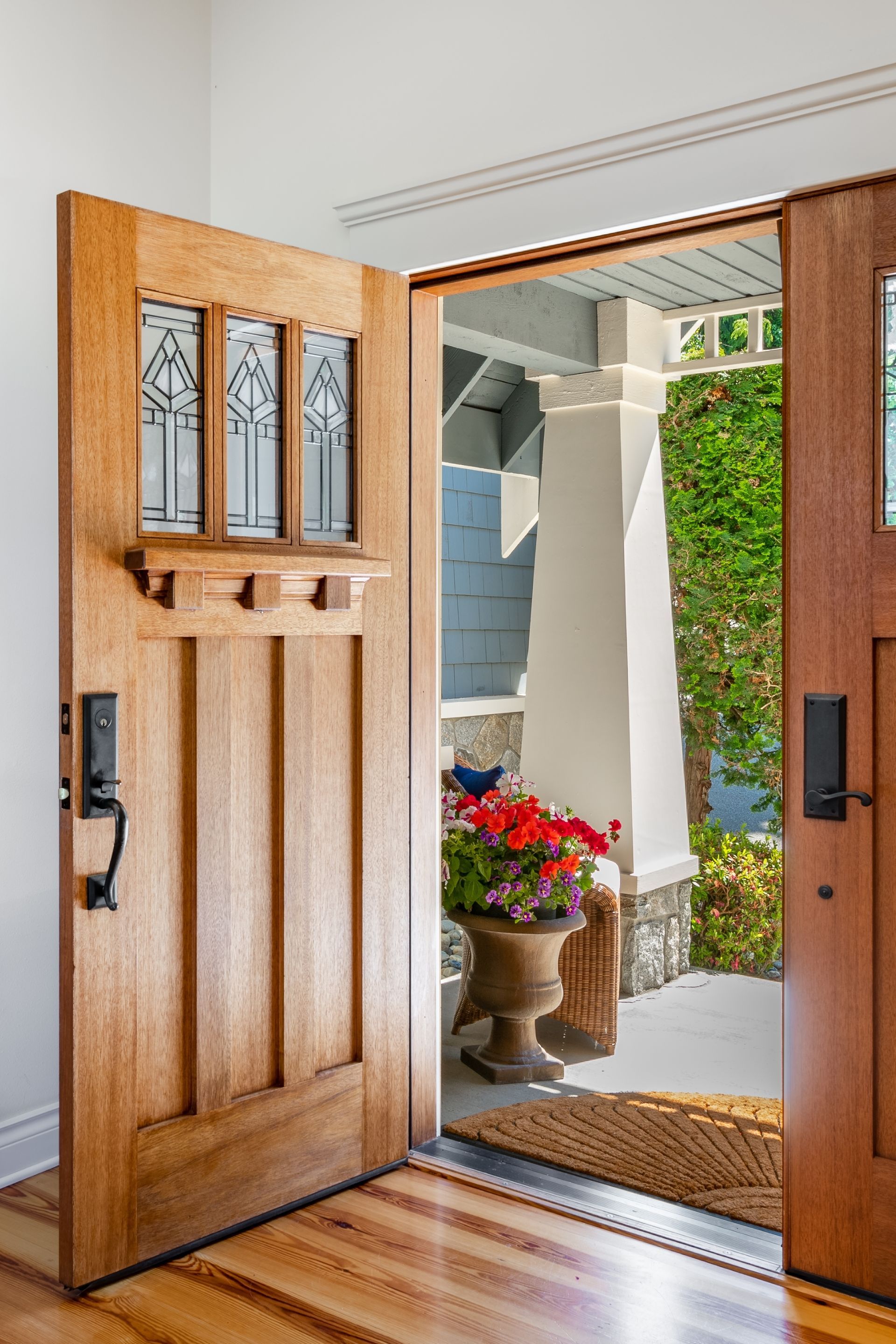 A wooden door is open to a porch with flowers in a vase.