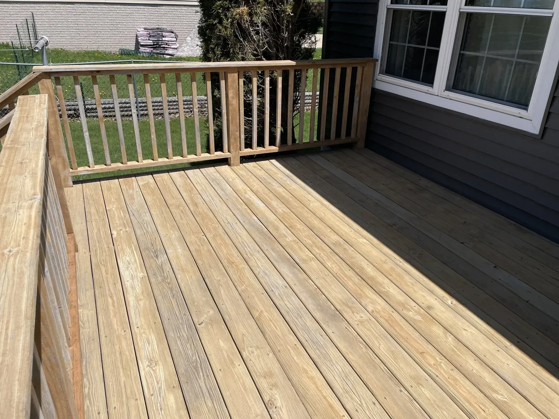 A wooden deck with railing attached to the side of a grey-sided house, viewed from an elevated angle.
