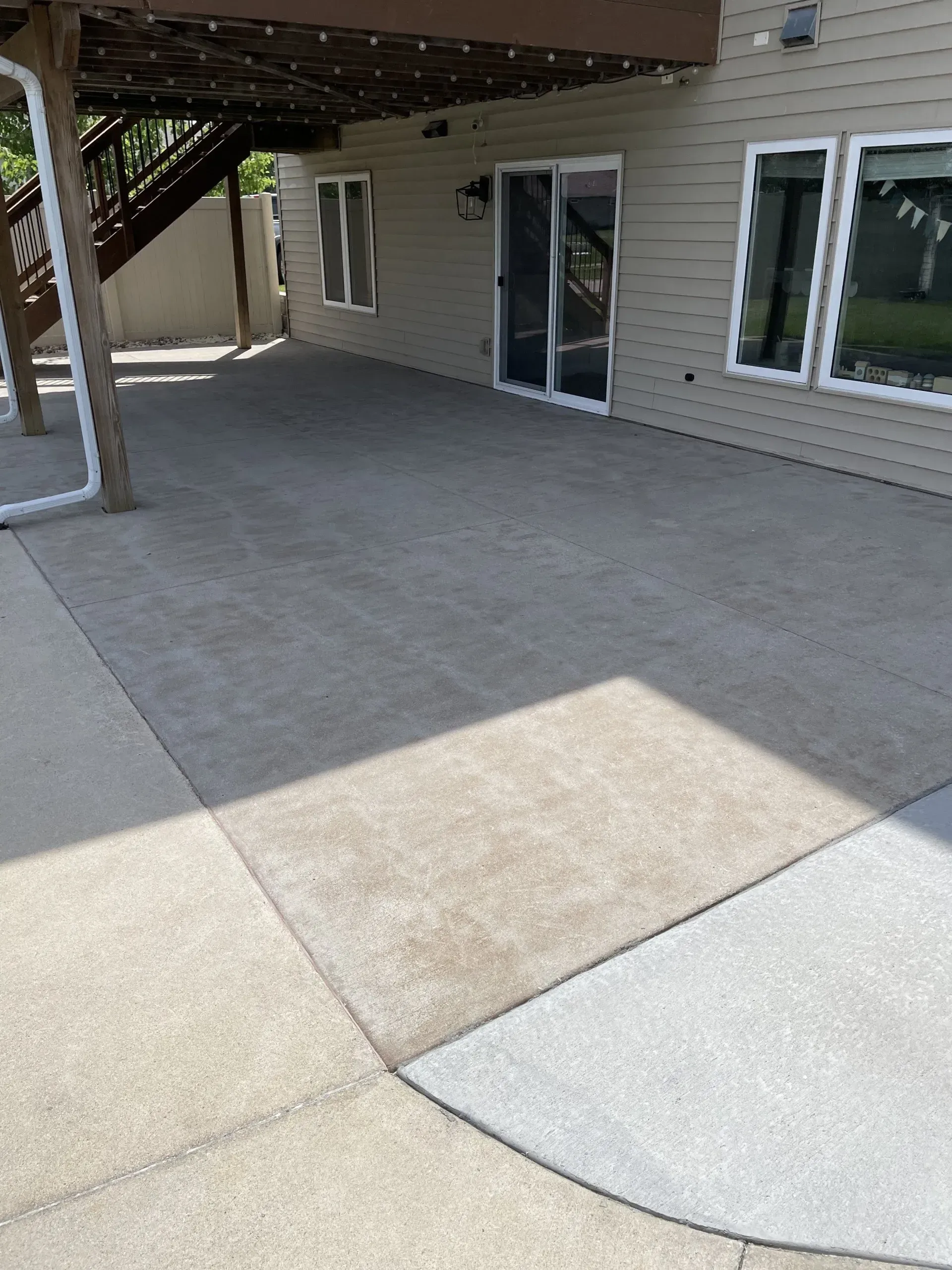 A concrete patio area beneath an elevated deck, featuring a glass sliding door and beige siding on a house exterior.