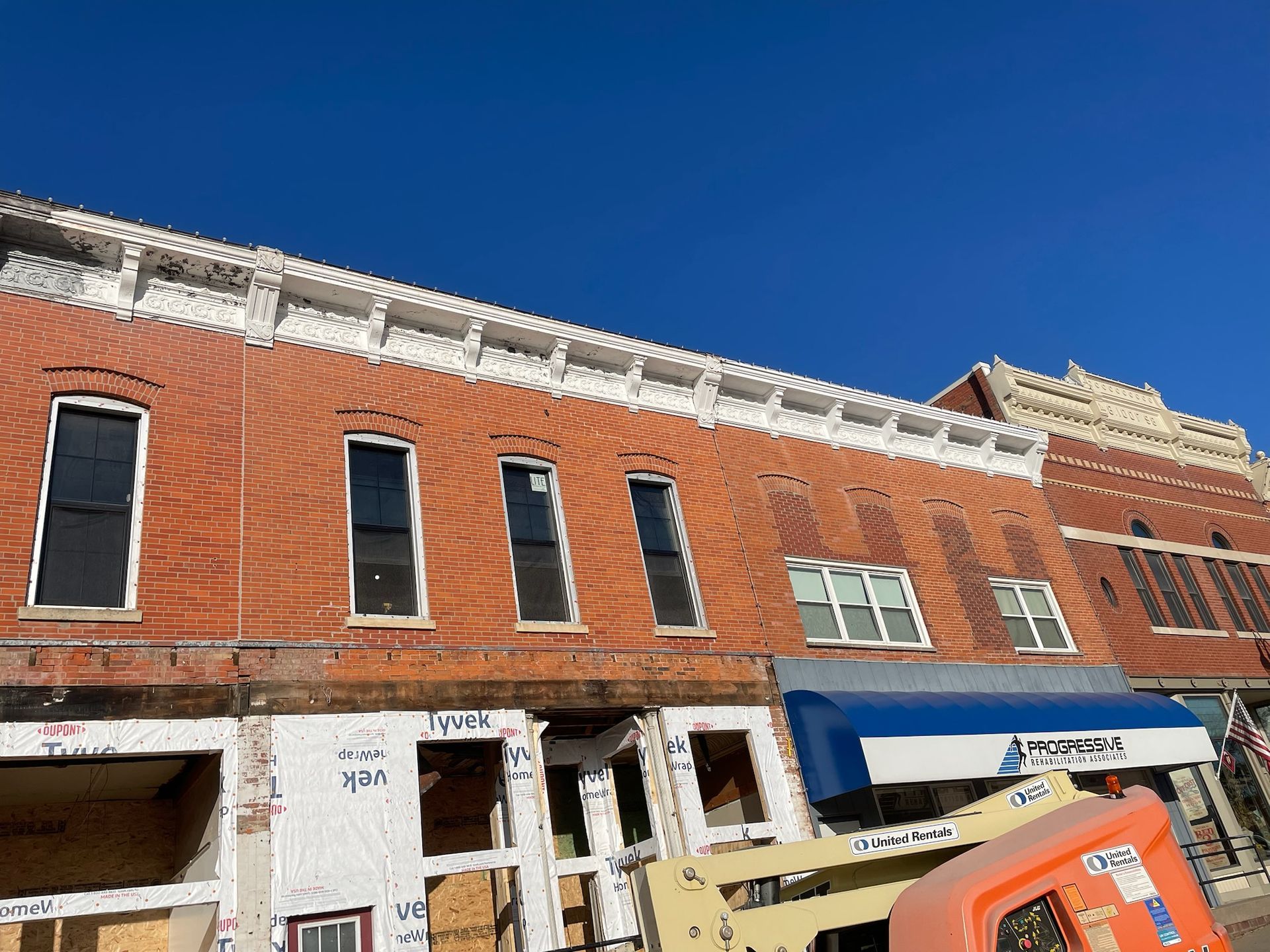 A multi-story brick commercial building under renovation with exposed structural frames, white trim, and a blue awning.